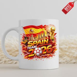 K&ouml;nnte beinhalten: Wei&szlig;e Keramik-Tasse mit einem lebendigen Design f&uuml;r das spanische Team im Jahr 2026. Das Design zeigt die spanische Flagge, einen Fu&szlig;ball und den Text "SPAIN TEAM 2026". Ein "Best Seller"-Tag ist sichtbar.