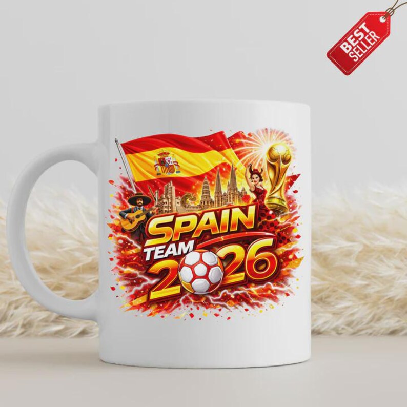K&ouml;nnte beinhalten: Wei&szlig;e Keramik-Tasse mit einem lebendigen Design f&uuml;r das spanische Team im Jahr 2026. Das Design zeigt die spanische Flagge, einen Fu&szlig;ball und den Text "SPAIN TEAM 2026". Ein "Best Seller"-Tag ist sichtbar.