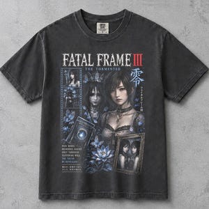 May include: A charcoal grey short-sleeve t-shirt featuring a graphic print from Fatal Frame III: The Tormented. The design includes character illustrations, a camera, blue flowers, butterflies, and text that reads: Pain binds, memories haunt, only through suffering will the truth be revealed.