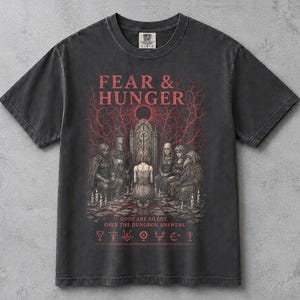 Könnte beinhalten: Ein anthrazitfarbenes Kurzarm-T-Shirt mit einem roten Grafikdruck und dem Text FEAR & HUNGER, GODS ARE SILENT. ONLY THE DUNGEON ANSWERS. Das Design zeigt eine zentrale Figur, die vor einem steinernen Torbogen kniet, umgeben von verschiedenen Charakteren.