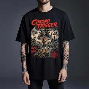 May include: A black t-shirt featuring a graphic print with the red text "CHRONO TRIGGER" at the top. The design depicts a character with spiky red hair holding a sword, standing before a dark castle and a large moon. Text reads "TIME WAITS FOR NO ONE. WHAT WILL YOU FIGHT FOR?"