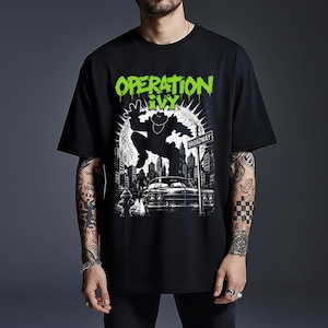 以下が含まれることがあります： 鮮やかなグリーンの「OPERATION IVY」というテキストがプリントされた黒の半袖Tシャツ。デザインには、車、消火栓、ブロードウェイの道路標識がある街の通りを飛び越える人物のシルエットが描かれています。