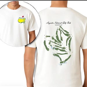May include: White t-shirt featuring a Masters logo on the front and a golf course map on the back. The front logo includes a yellow map outline with the word "Masters" and a red flag. The back of the shirt has the text "Augusta National Golf Club, Augusta, GA".