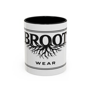 Può includere: Tazza in ceramica bianca con interno nero. La tazza presenta la parola "BROOT" in nero, sopra un disegno di radice di albero. La parola "WEAR" è sotto, il tutto all'interno di un bordo con linee nere.