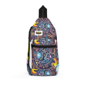 Könnte beinhalten: Ein Sling-Rucksack mit einem farbenfrohen, geometrischen Design mit Pac-Man-Charakteren und einem labyrinthartigen Muster. Die Tasche hat einen schwarzen Riemen und Reißverschluss, mit einem weißen Akzent an der Seite. Der Markenname "Brood" ist sichtbar.