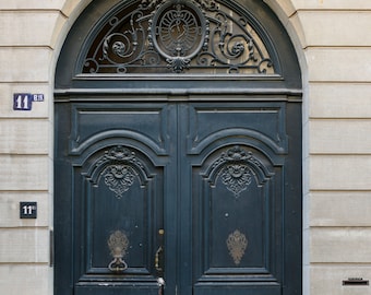 May include: A dark blue double door with ornate metalwork above the door and decorative carvings on the door panels. The door is set in a stone archway with a stone sculpture above the archway. The door has two numbers on it: "11" and "11 bis".