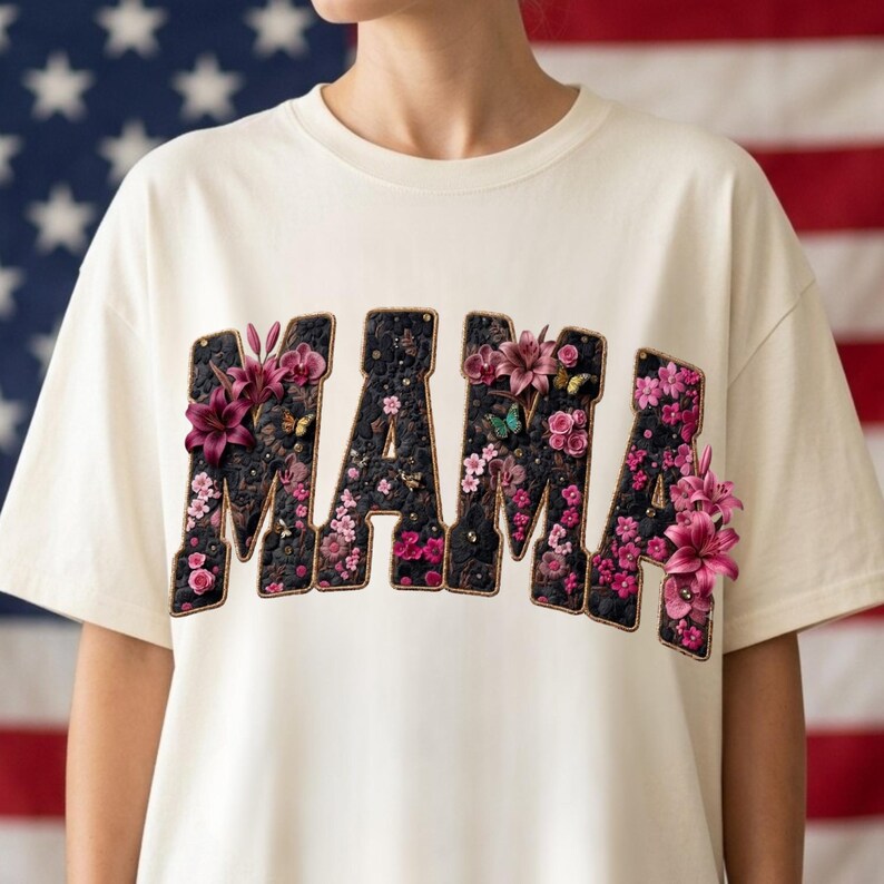 Pu&ograve; includere: Una t-shirt color crema con la parola MAMA in grandi lettere in stile blocco. Le lettere sono riempite con un motivo floreale scuro e testurizzato, accentuato da gigli rosa tridimensionali, piccoli fiori rosa e minuscole farfalle.