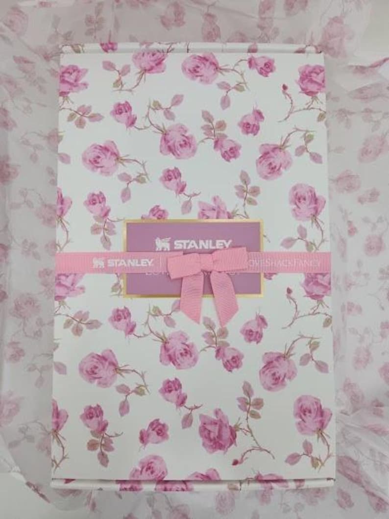 May include: A rectangular gift box with a floral rose pattern in pink and white. The box is wrapped with a pink ribbon and bow. The brand name "STANLEY" is visible on the box.