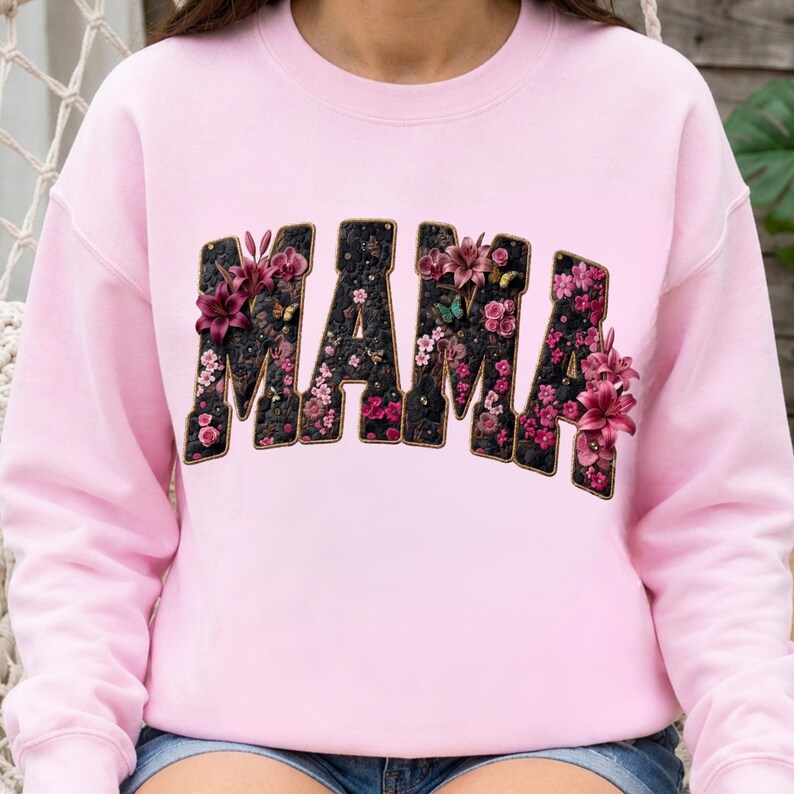 Pu&ograve; includere: Una felpa girocollo rosa chiaro con la parola MAMA in grandi lettere in stile blocco. Le lettere hanno uno sfondo nero testurizzato riempito con una variet&agrave; di motivi floreali rosa e viola, inclusi gigli e piccoli fiori.