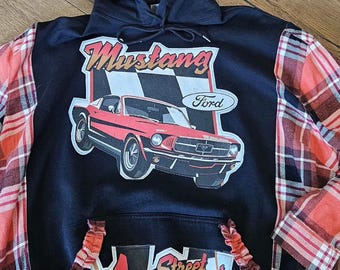 Puede incluir: Sudadera con capucha negra con un gráfico de coche Mustang rojo y el logotipo de Ford. Las mangas son de tela a cuadros roja, negra y blanca. El bolsillo delantero tiene el texto "Street Legend".
