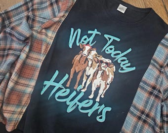 Puede incluir: Sudadera negra con mangas a cuadros. La parte delantera presenta el texto turquesa "Not Today Heifers" y un gráfico de tres vacas. Las mangas a cuadros combinan azul, naranja y marrón.
