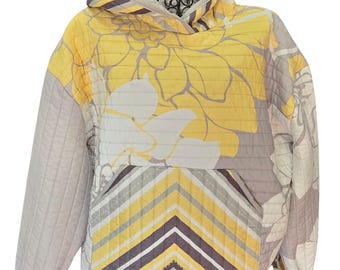 Puede incluir: Una sudadera con capucha acolchada en tonos amarillos, grises y blancos, con un estampado floral en la capucha y la parte superior del cuerpo. La sección inferior tiene un diseño de chevron. Las mangas son de color gris sólido y tiene un bolsillo delantero.