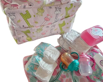 Puede incluir: Un juego de cuidado del bebé con un bolso tote rosa y blanco con estampado de jirafas, pañales, biberones, un chupete y un cambiador. El juego incluye un recipiente para toallitas rosa y una cuchara para bebé amarilla.