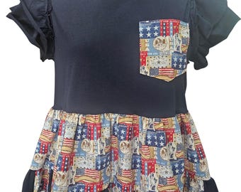 Puede incluir: Una camiseta negra de manga corta con volantes y un bolsillo con estampado patriótico. La parte inferior de la camiseta tiene un dobladillo de volantes a juego con un patrón en rojo, blanco y azul que muestra banderas, estrellas y texto.