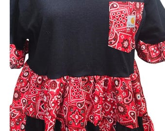 Puede incluir: Vestido camiseta negro con falda y bolsillo con estampado de cachemira rojo. El bolsillo tiene un logotipo de Carhartt. El vestido tiene mangas cortas con puños de cachemira y una falda escalonada. El vestido se muestra en un maniquí.