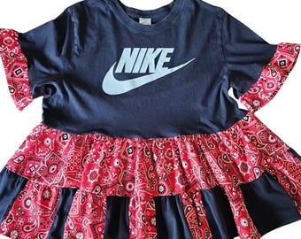 Puede incluir: Vestido camiseta azul marino con el logo Nike blanco. El vestido presenta mangas con volantes con estampado de cachemira rojo y una falda escalonada. Un diseño único y elegante.