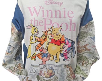 Puede incluir: Una sudadera de manga larga con un panel central color crema que presenta un gráfico de Winnie the Pooh y sus amigos, incluidos Tigger, Piglet, Roo y Eeyore. El texto dice Disney Winnie the Pooh. Las mangas y el bolsillo delantero tienen un patrón.