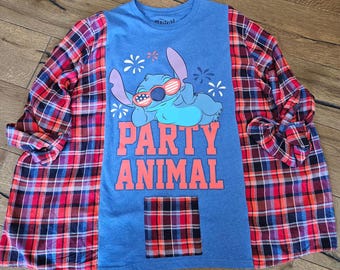 Puede incluir: Una camiseta azul con un gráfico de Stitch con gafas de sol y las palabras "PARTY ANIMAL" en naranja. La camiseta se combina con una camisa de franela a cuadros roja, negra y azul. Un pequeño bolsillo a cuadros está cosido en la parte delantera.