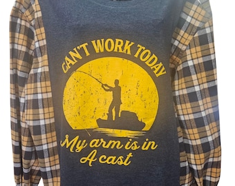 Puede incluir: Una camiseta de manga larga con cuerpo gris oscuro y mangas a cuadros en negro, amarillo y blanco. La camiseta presenta un círculo amarillo con una escena de pesca y el texto "CAN'T WORK TODAY" y "My arm is in A cast."