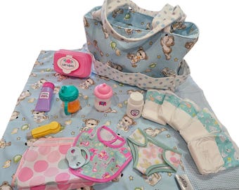Puede incluir: Un bolso de mano azul claro con estampado de ositos, una caja de toallitas húmedas rosa, un frasco de loción morado, un vaso de aprendizaje turquesa, un biberón rosa, un frasco blanco, una herramienta amarilla, un babero rosa, un chupete y pañales.
