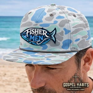 May include: A camouflage-patterned baseball cap in shades of blue, gray, and white. The cap features a patch with the words "FISHER OF MEN" and a fish graphic. The brim is flat, and the cap has a rope detail. The brand "GOSPEL HABITS APPAREL" is also visible.