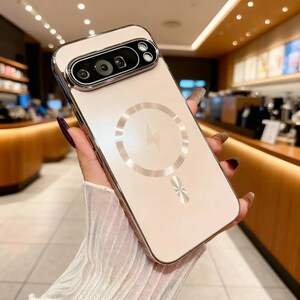 May include: A pale pink phone case with a metallic gold trim and camera section. The back has a circular design with a lightning bolt symbol, and a decorative element. The case is designed for a smartphone.