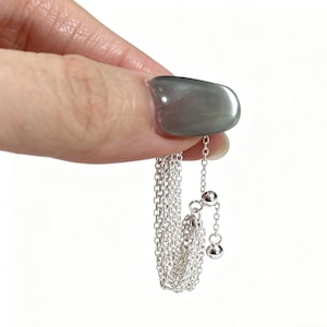 Könnte beinhalten: Eine zarte Silberkette mit feiner Kette und zwei kleinen, runden Anhängern. Die Halskette wird vor einem weißen Hintergrund gehalten, was ihre schlichte Eleganz und ihr Potenzial zum Kombinieren mit anderem Schmuck unterstreicht.