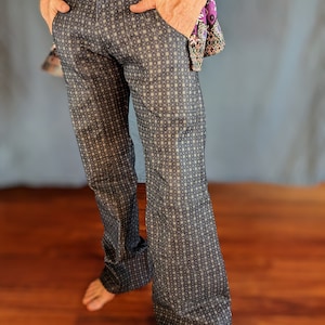 May include: Dark blue patterned pants with a repeating geometric design. The pants have a button closure and pockets. The fabric has a subtle sheen. The pants are flared at the bottom.