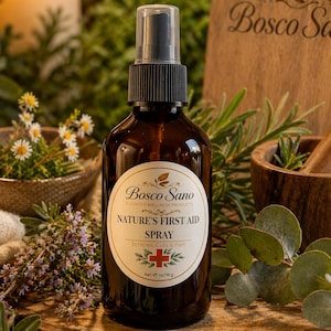 Pode incluir: Uma garrafa de spray de vidro castanho com tampa preta e rótulo branco que diz "Nature's First Aid Spray" da Bosco Sano. A garrafa está sobre uma superfície de madeira, rodeada por vegetação, uma vela acesa e uma pequena tigela de flores. Contém 118 g.