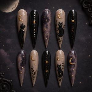 May include: A set of ten stiletto-shaped press-on nails featuring celestial and feline designs. The nails display black cats, gold crescent moons, stars, and botanical motifs against black, beige, and purple galaxy-patterned backgrounds.