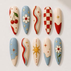 Pode incluir: Um conjunto de dez unhas postiças em formato de amêndoa com vários designs, incluindo cerejas vermelhas, flores brancas, padrões xadrez vermelhos e brancos, sóis dourados e estrelas em tons de creme, azul celeste e vermelho vibrante.