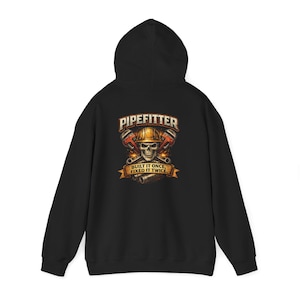Puede incluir: Sudadera con capucha negra con un gráfico en la espalda. El gráfico presenta una calavera con un casco, llaves inglesas cruzadas y el texto "PIPEFITTER" y "BUILT IT ONCE, FIXED IT TWICE" en una pancarta.