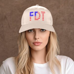 May include: A cream-colored baseball cap with the letters "FDT" in red and blue, designed to resemble the American flag. The hat has a curved brim and a classic six-panel design.