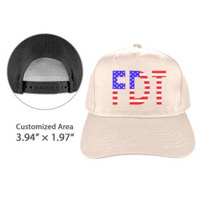 May include: A beige baseball cap with the letters "FDT" in red, white, and blue. The letters are designed to resemble the American flag. The cap has a black adjustable snapback closure.