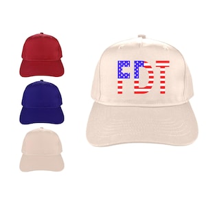 May include: A cream-colored baseball cap with the letters "FDT" in red and blue, designed to resemble the American flag. Three additional baseball caps in red, blue, and cream are also visible.