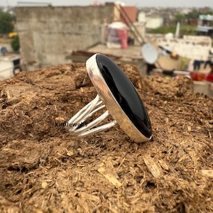 May include: A silver ring featuring a large, oval, black onyx gemstone. The ring has a multi-band design. The ring is set against a textured, brown surface. A bold piece of jewellery.