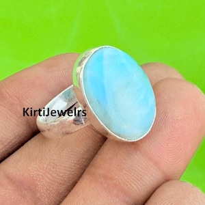 Könnte beinhalten: Ein Silberring mit einem großen, ovalen, hellblauen Edelstein. Der Ring hat ein schlichtes, poliertes Band, und der Edelstein hat eine glatte, polierte Oberfläche. Der Text "KirtiJewelrs" ist auf dem Ring zu sehen.
