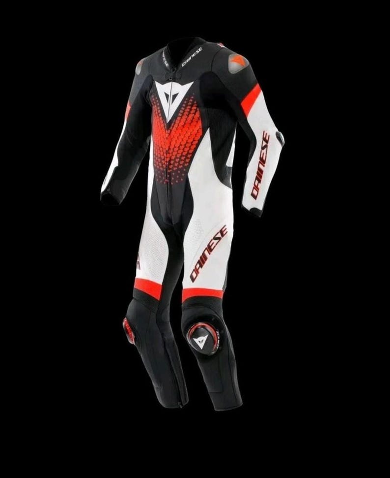 May include: A black, white, and red motorcycle racing suit. The suit features white panels on the arms and legs, with red accents and the brand name "DAINESE" printed on the arms and legs. The suit has a front zipper and protective padding.