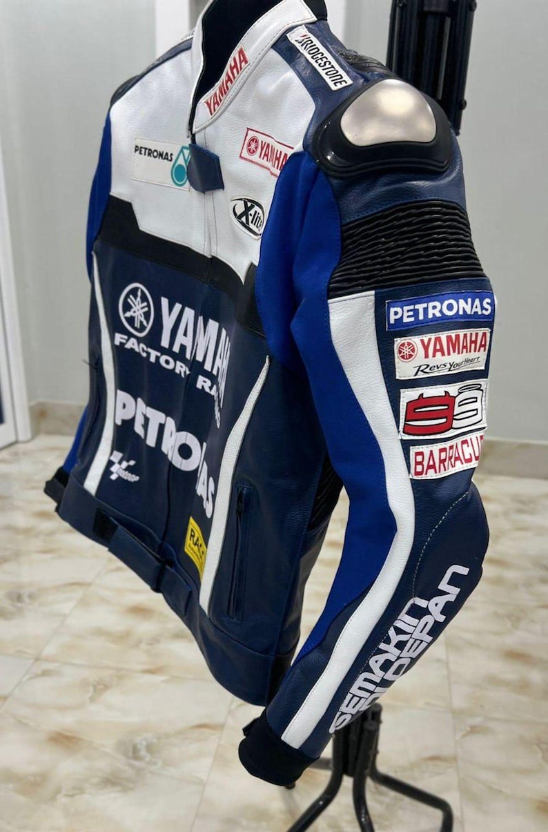 Puede incluir: Una chaqueta de cuero para motocicleta en azul, blanco y negro con logotipos de Yamaha Factory Racing, Petronas y Bridgestone. La chaqueta incluye un protector de hombro plateado, bolsillos con cremallera y varios logotipos de patrocinadores.