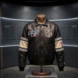 Peut inclure: Veste en cuir noire avec les logos "Avirex" et "NFL". La veste a des rayures blanches et grises sur les manches et une fermeture boutonn&eacute;e. La veste est pr&eacute;sent&eacute;e sur un mannequin.