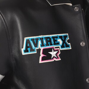 Peut inclure: Veste en cuir noire avec des &eacute;cussons "AVIREX" et "Starter". L'&eacute;cusson "AVIREX" a un contour bleu, et l'&eacute;cusson "Starter" pr&eacute;sente une &eacute;toile blanche. La veste a une fermeture &agrave; boutons-pression et une bordure blanche.