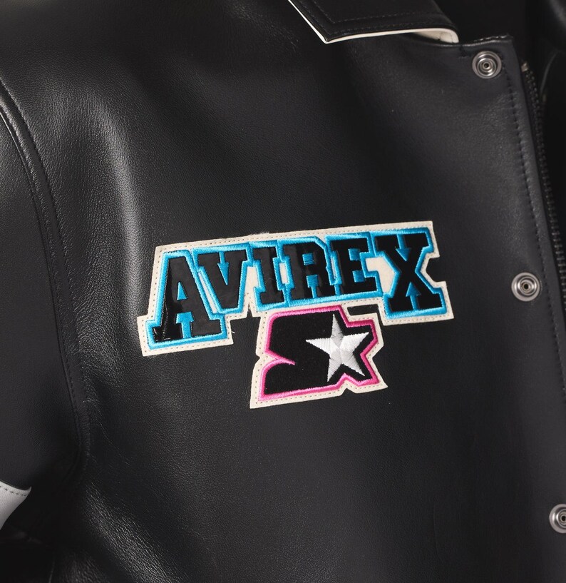 Peut inclure: Veste en cuir noire avec des &eacute;cussons "AVIREX" et "Starter". L'&eacute;cusson "AVIREX" a un contour bleu, et l'&eacute;cusson "Starter" pr&eacute;sente une &eacute;toile blanche. La veste a une fermeture &agrave; boutons-pression et une bordure blanche.