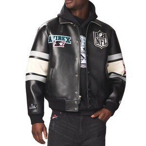 Peut inclure: Veste en cuir noire avec des rayures blanches et grises sur les manches. Comporte le logo "NFL" et l'&eacute;cusson "AVIREX". La veste a un col et des poignets c&ocirc;tel&eacute;s, et une fermeture &eacute;clair.