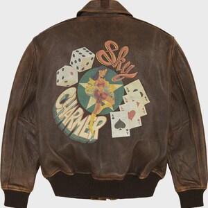 May include: Brown leather bomber jacket with a graphic on the back featuring dice, playing cards, and a pin-up girl. The text "Sky Charmer" is also displayed. The jacket has a ribbed collar and cuffs.