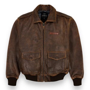 May include: A brown leather bomber jacket with a zip-up front, two front pockets, and a ribbed hem and cuffs. The jacket has a distressed appearance and the brand name "AVIREX" is visible.