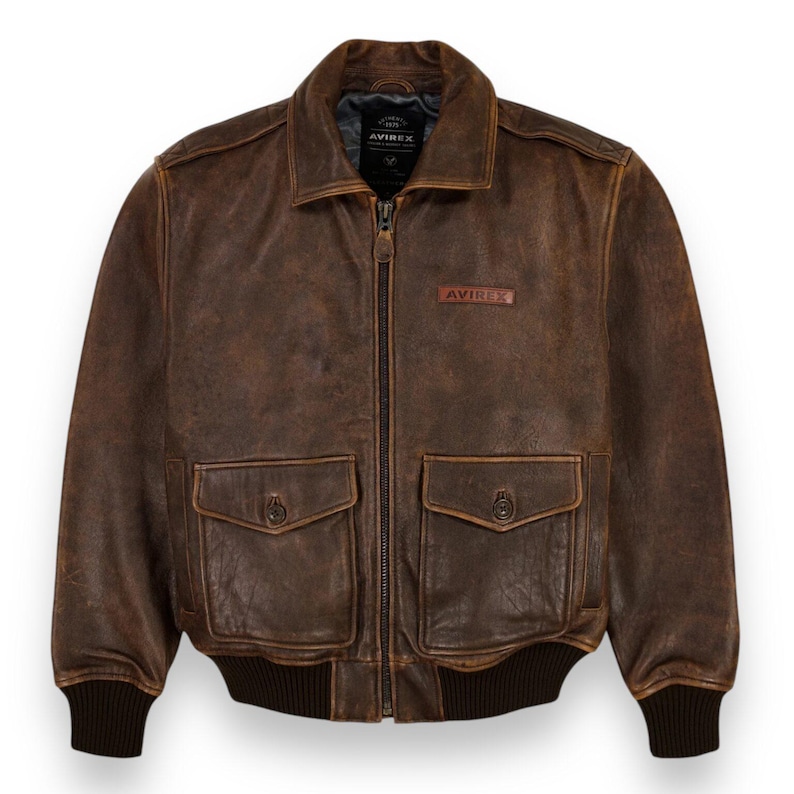May include: A brown leather bomber jacket with a zip-up front, two front pockets, and a ribbed hem and cuffs. The jacket has a distressed appearance and the brand name "AVIREX" is visible.