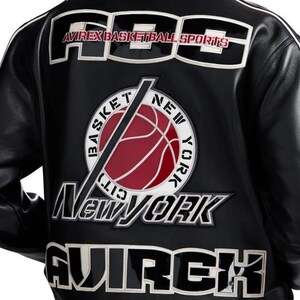 Może przedstawiać: Czarna sk&oacute;rzana kurtka z dużymi białymi i czarnymi haftowanymi naszywkami na plecach. Napis głosi ABS AVIREX BASKETBALL SPORTS, BASKET NEW YORK CITY, NEW YORK oraz AVIREX. Centralna okrągła naszywka przedstawia czerwoną piłkę do koszyk&oacute;wki.