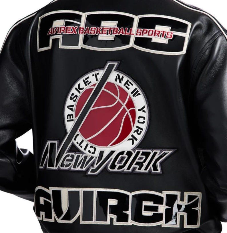 Może przedstawiać: Czarna sk&oacute;rzana kurtka z dużymi białymi i czarnymi haftowanymi naszywkami na plecach. Napis głosi ABS AVIREX BASKETBALL SPORTS, BASKET NEW YORK CITY, NEW YORK oraz AVIREX. Centralna okrągła naszywka przedstawia czerwoną piłkę do koszyk&oacute;wki.