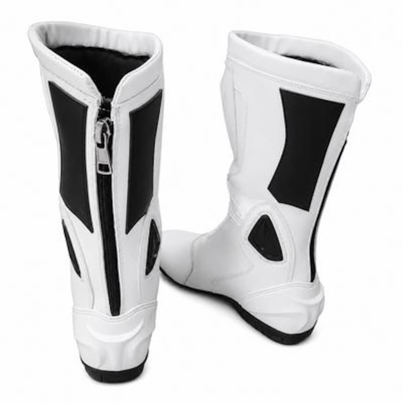 K&ouml;nnte beinhalten: Paar wei&szlig;-schwarze Motorradstiefel. Die Stiefel haben ein hohes Design mit Rei&szlig;verschluss und schwarzen Akzenten an den Seiten. Die Sohlen sind schwarz und die Stiefel scheinen aus einem synthetischen Material zu sein.