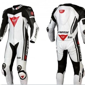 Puede incluir: Traje de carreras de moto blanco y negro con detalles en rojo. El traje presenta un logotipo triangular rojo en el pecho y la espalda, con la marca "Dainese" visible. Incluye protectores de rodillas y codos.